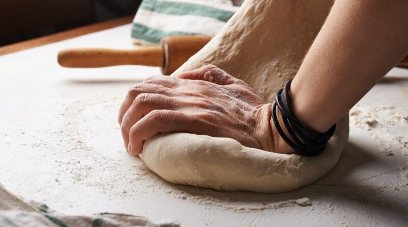 person making dough beside brown wooden rolling pin