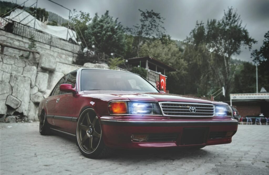 A classic luxury sedan with bright headlights parked on a paved outdoor area.