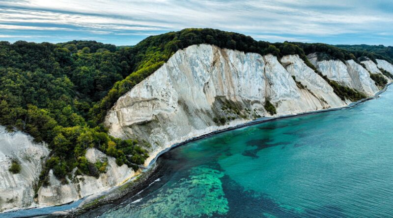 Stunning aerial view of white cliffs against a vibrant turquoise sea and lush greenery.